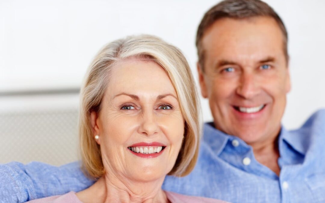 Smiling mature couple in blue shirts representing dental patients satisfied with their smile results.